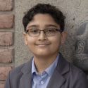 Rushi smiling in front of a brick background.