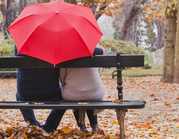 couple sitting on a park bench under red umbrella
