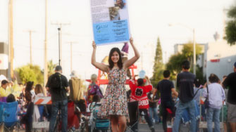 Girl standing outside holding a sign in front of  crowd of people behind her who are facing backwards.